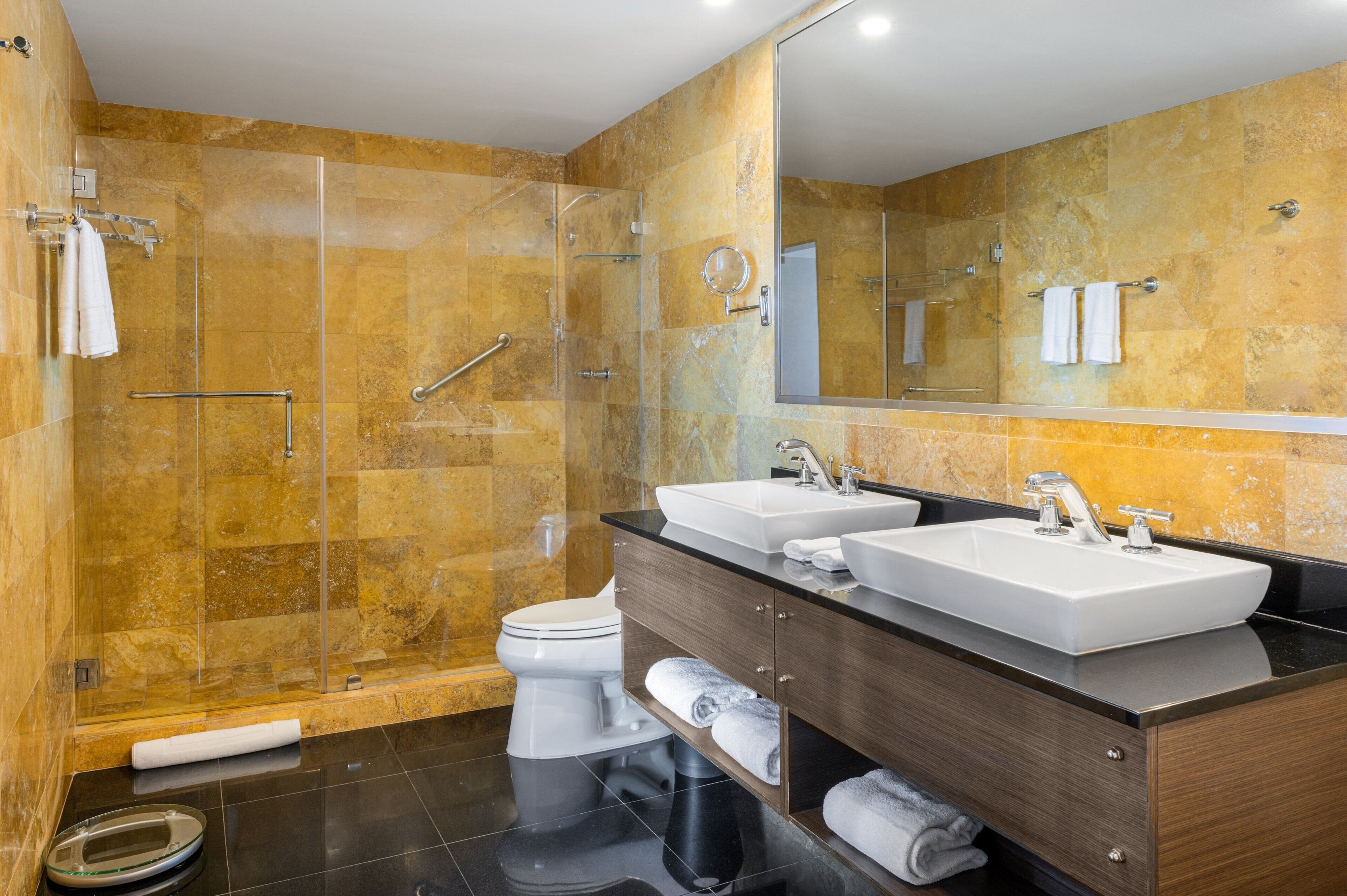 Une salle de bain moderne avec une douche à parois de verre, deux lavabos et un grand miroir.