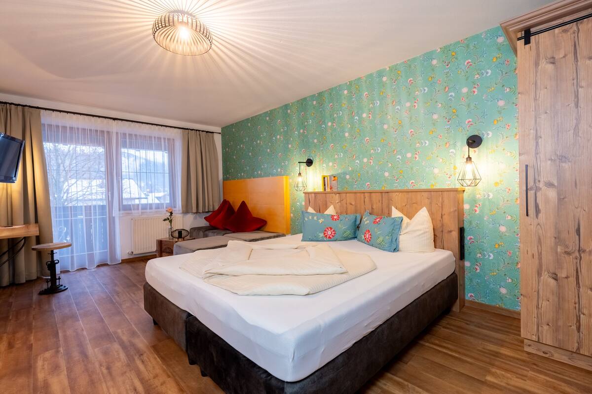 A bedroom with a large bed, a wooden headboard, a television, and a window with curtains.