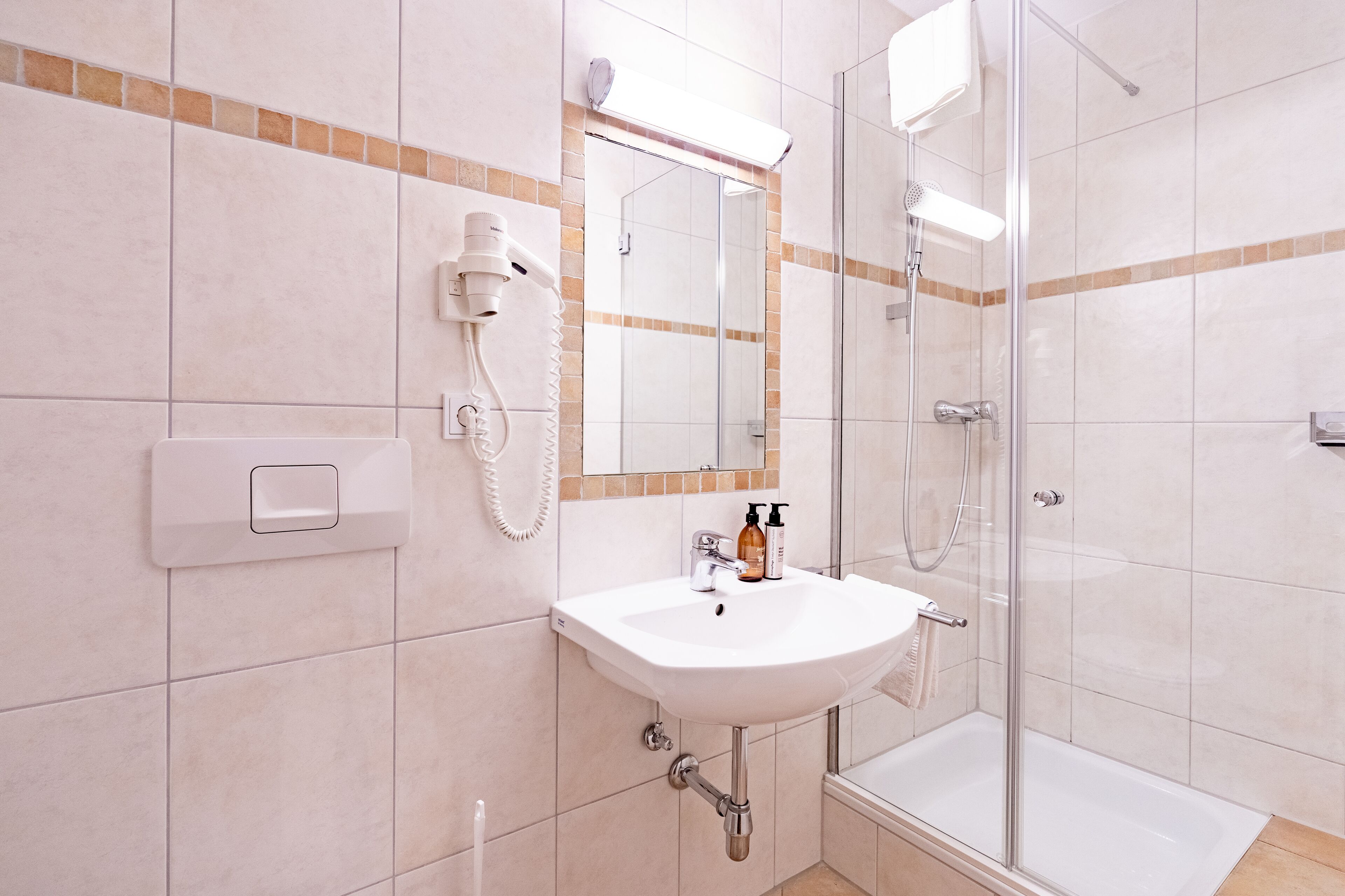 Un baño con lavamanos, espejo, secador de pelo y ducha.