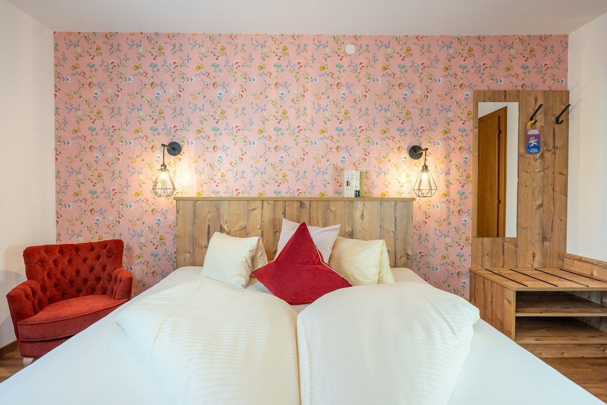 A double bed with white linens, a red chair, and a wooden headboard.