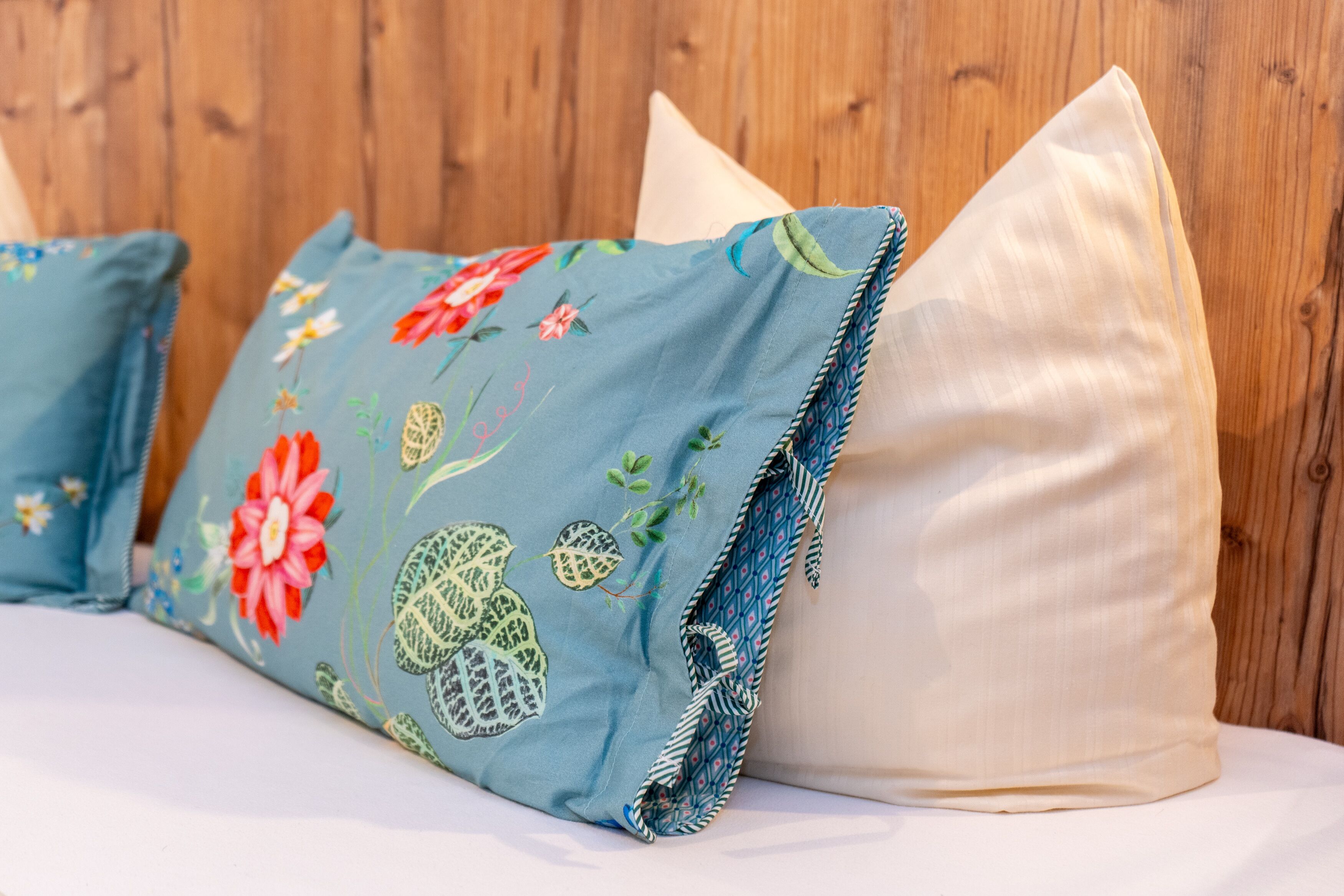 A bed with a floral pillow and a plain pillow against a wooden wall.