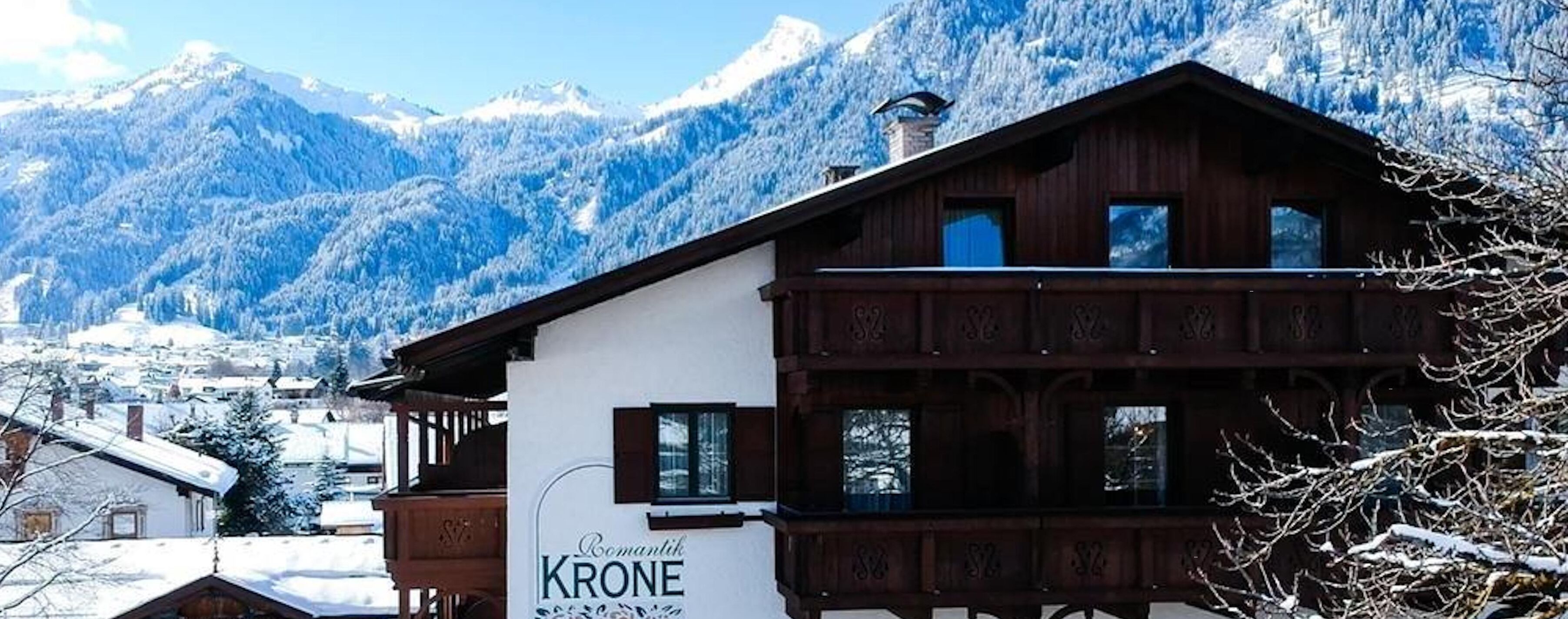 Ein traditionelles Holzhäuschen mit einem Schild, auf dem 'Romantik KRONE' steht, inmitten einer verschneiten Berglandschaft.