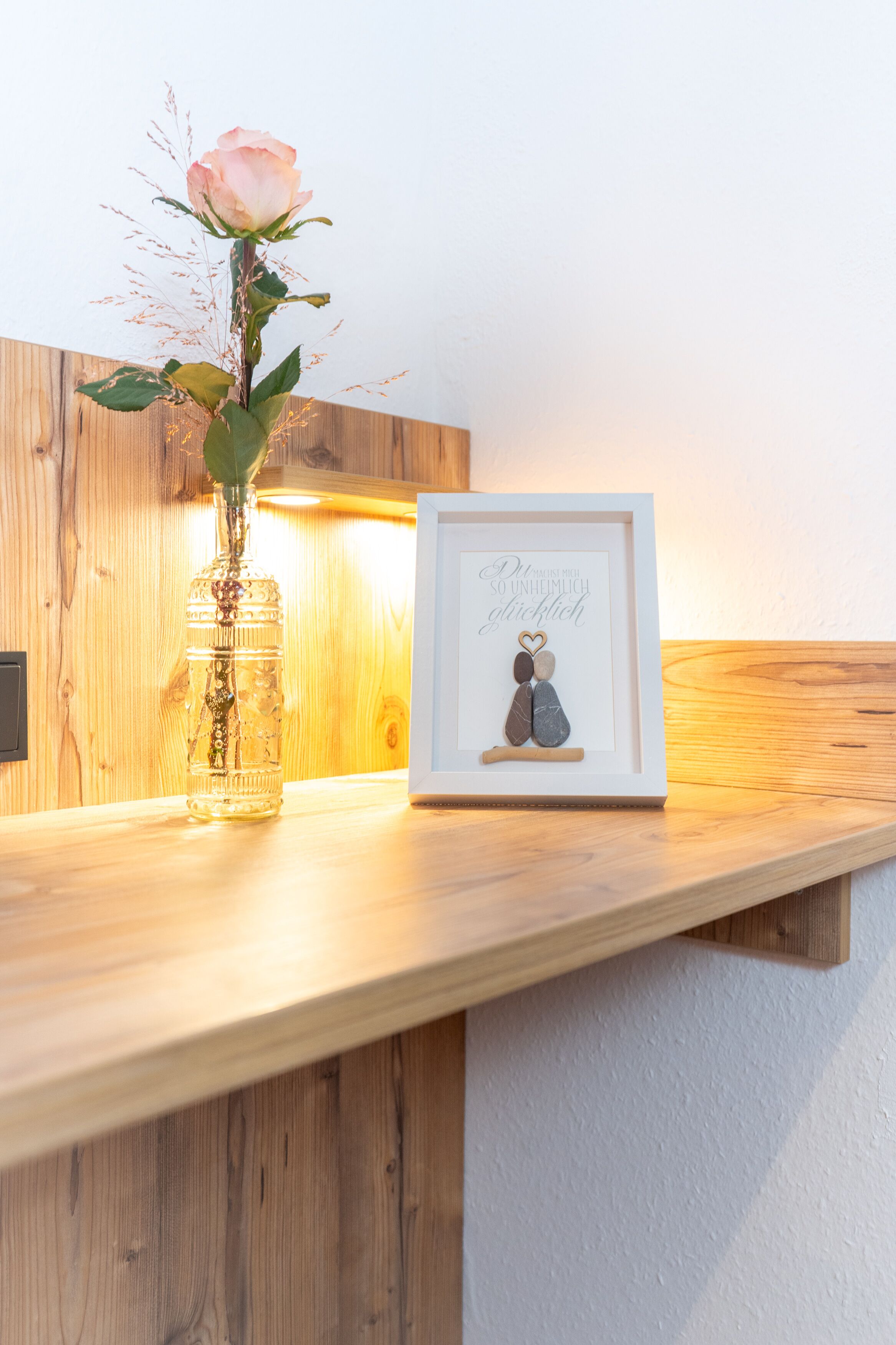 A wooden shelf with a glass vase containing a single rose and a framed picture of a couple.