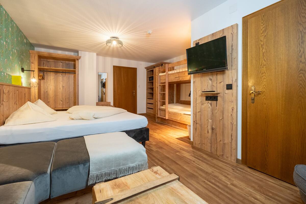 A bedroom with a bunk bed, wooden walls, a TV mounted on the wall, and a wooden door.