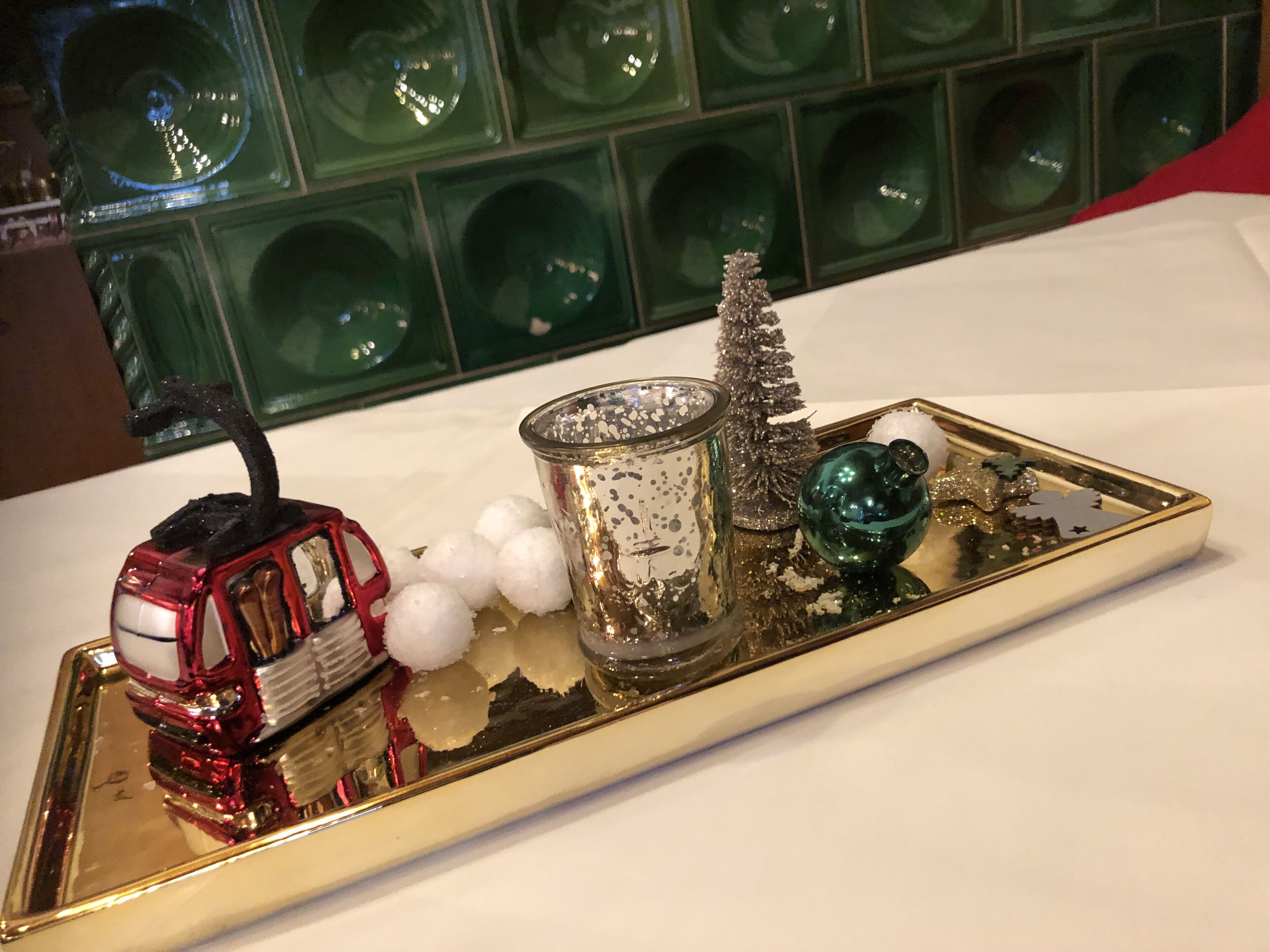 A tray with a red toy car, a glass container with snow-like decorations, a small Christmas tree, and a green ornament.