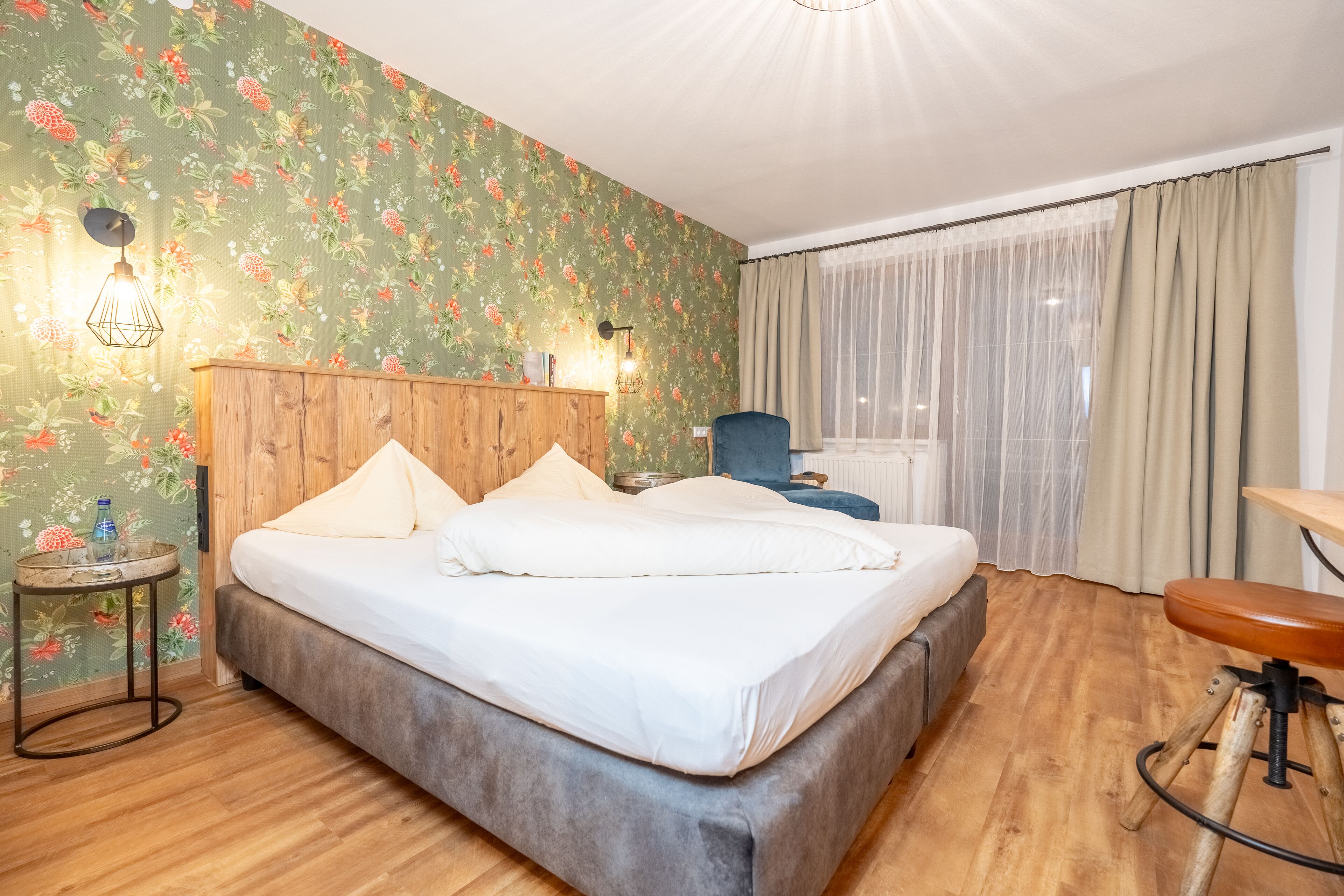 Habitación de hotel con cama de madera, una mesita redonda con lámpara, una silla y un escritorio con su propio asiento.