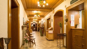 Zona de recepción de hotel con suelo de madera, mostrador de recepción, área de espera con sillas y un letrero de recepción.