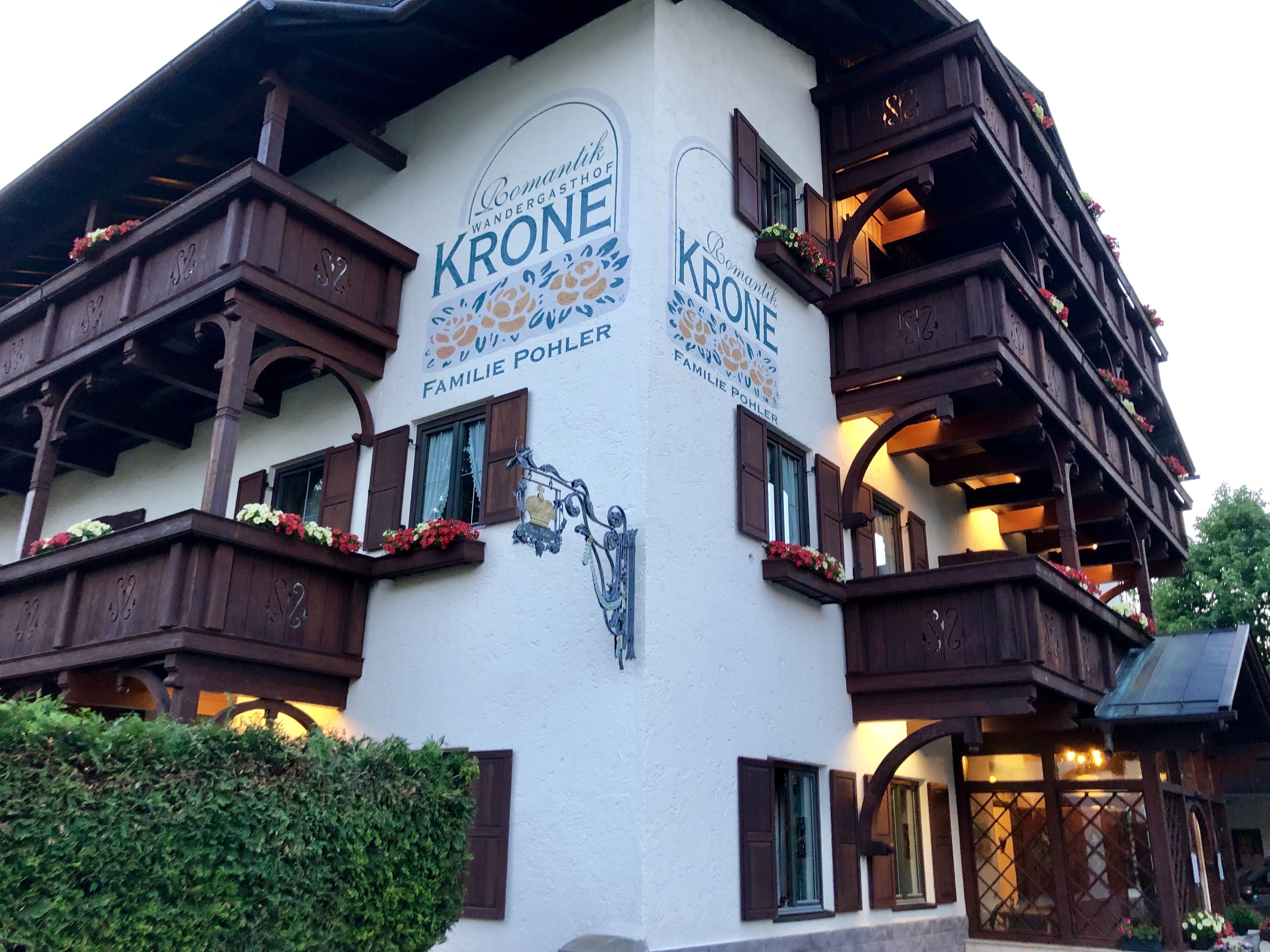 Un bâtiment dont la façade porte les inscriptions « Krone » et « Familie Pohler ». Il est doté de balcons en bois ornés de jardinières et présente un style architectural traditionnel.