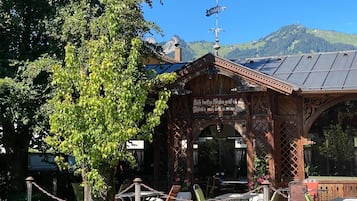A wooden gazebo with a sign, surrounded by potted plants and outdoor seating.