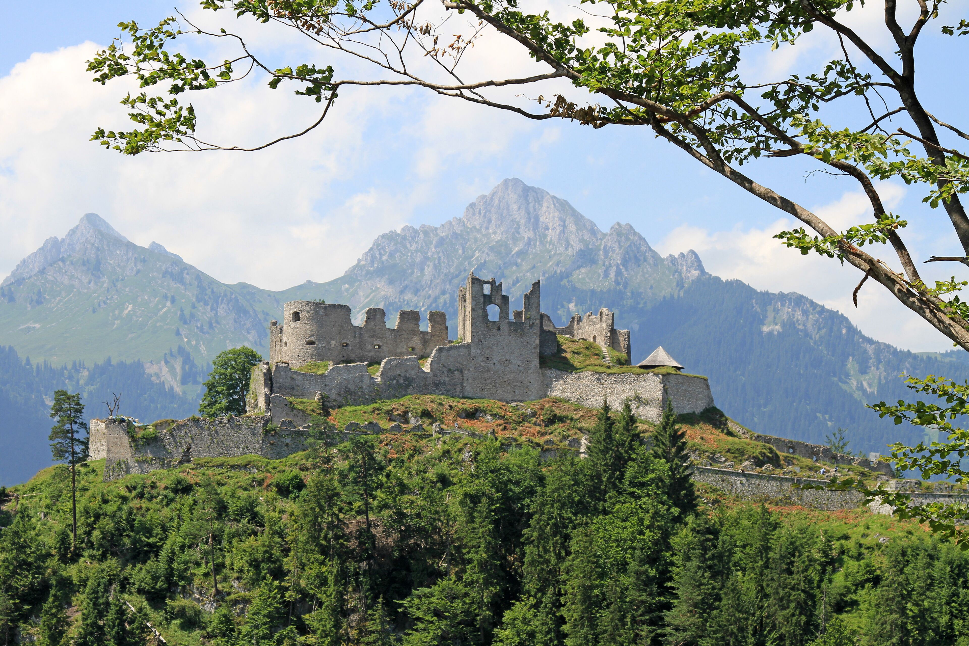 A historic castle on a hill with a mountainous backdrop.