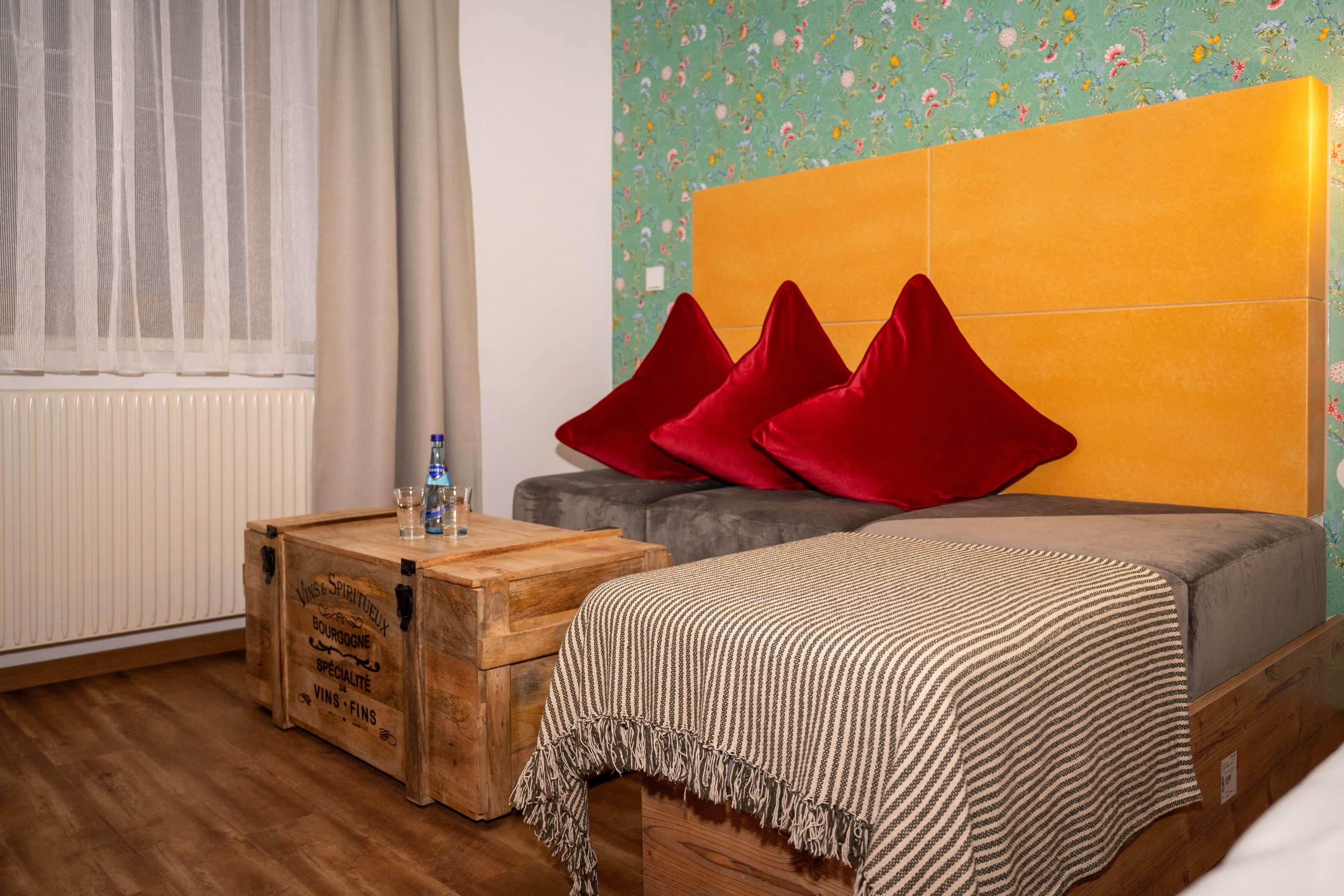 Ein Schlafzimmer mit einem Bett, einem Holz-Nachttisch, einer Heizung und einem Fenster mit transparenten Vorhängen.