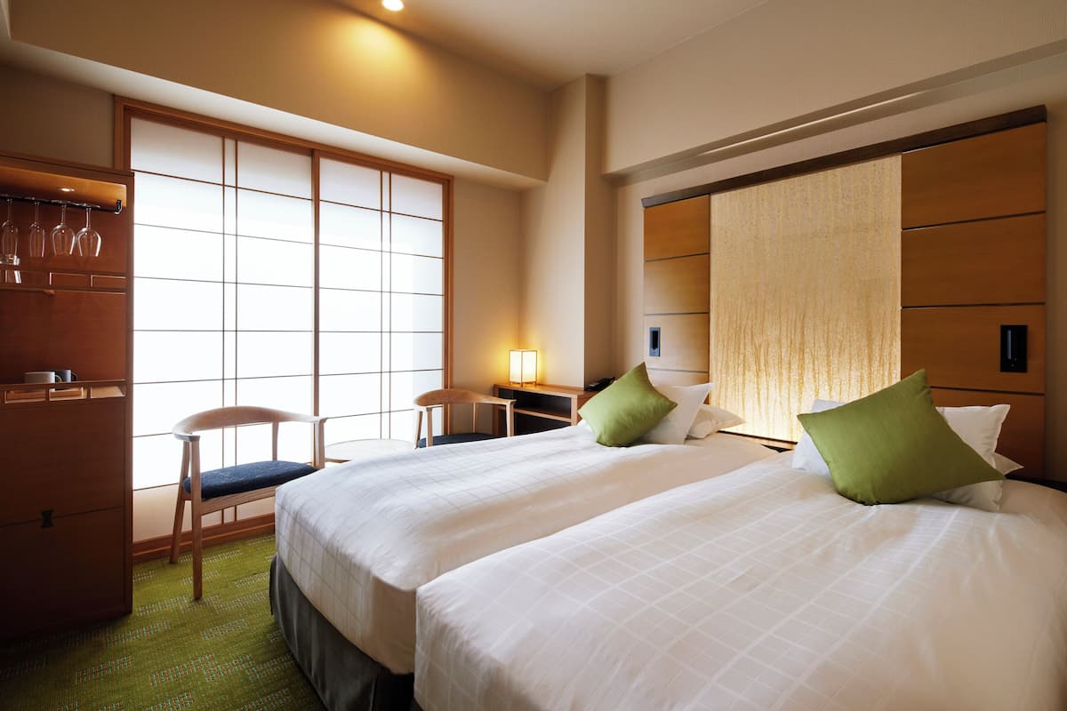 A hotel room with two beds, a desk, a chair, and a wardrobe.