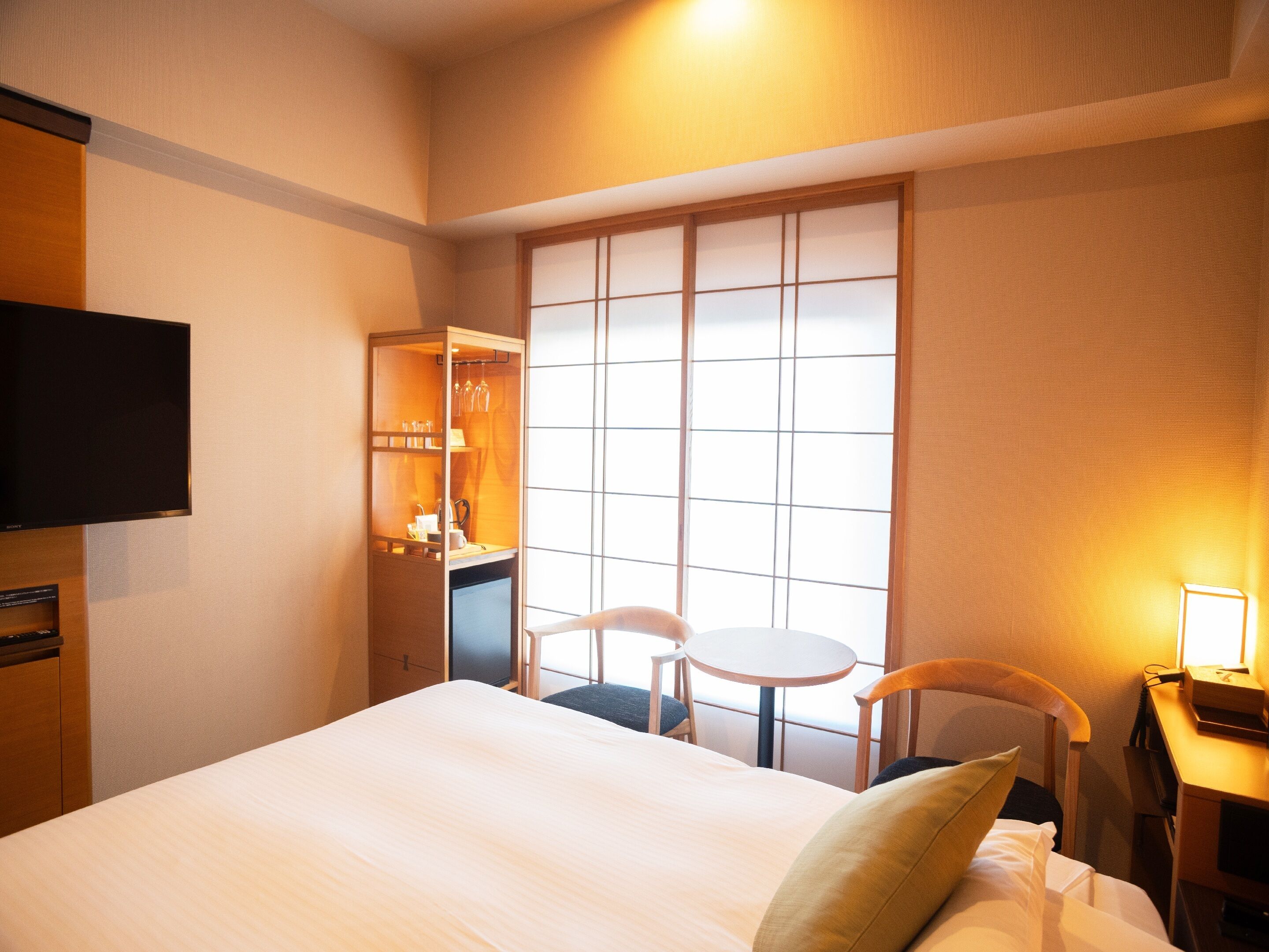 A hotel room with a bed, a desk with a chair, a TV, a wardrobe, and a window with a view.