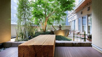 A wooden bench in a courtyard with bamboo plants and a tree.