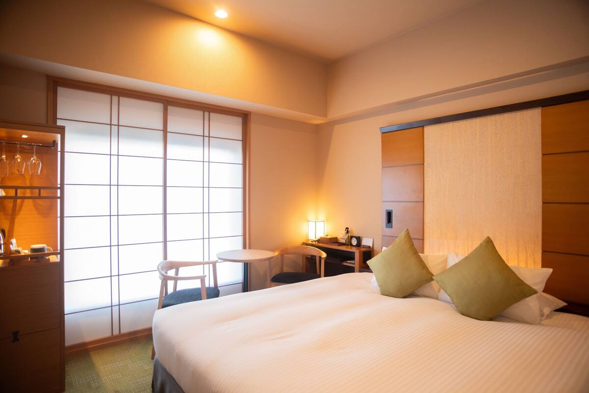 A hotel room with a bed, a desk, a chair, and a window with a view.