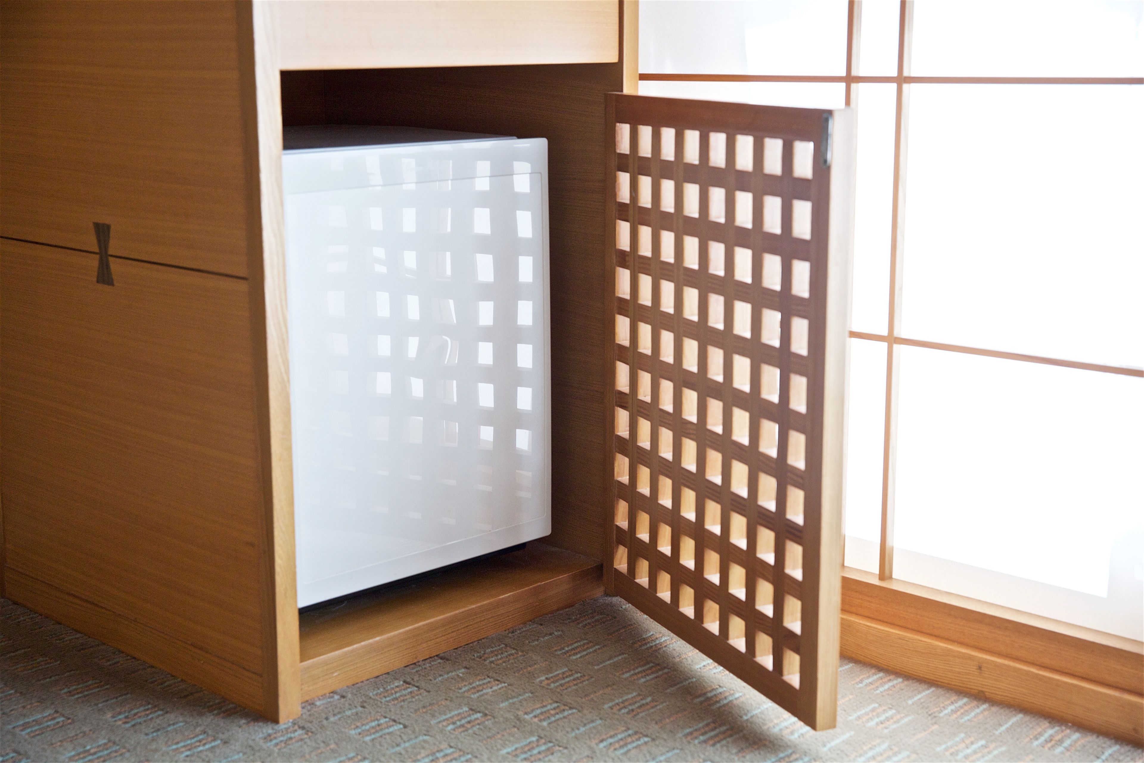 A wooden wardrobe with a built-in mini-fridge and a sliding door with a grid pattern.