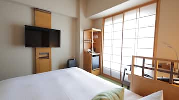 Habitación de hotel con cama, televisor montado en la pared, armario y puerta corredera con vistas.