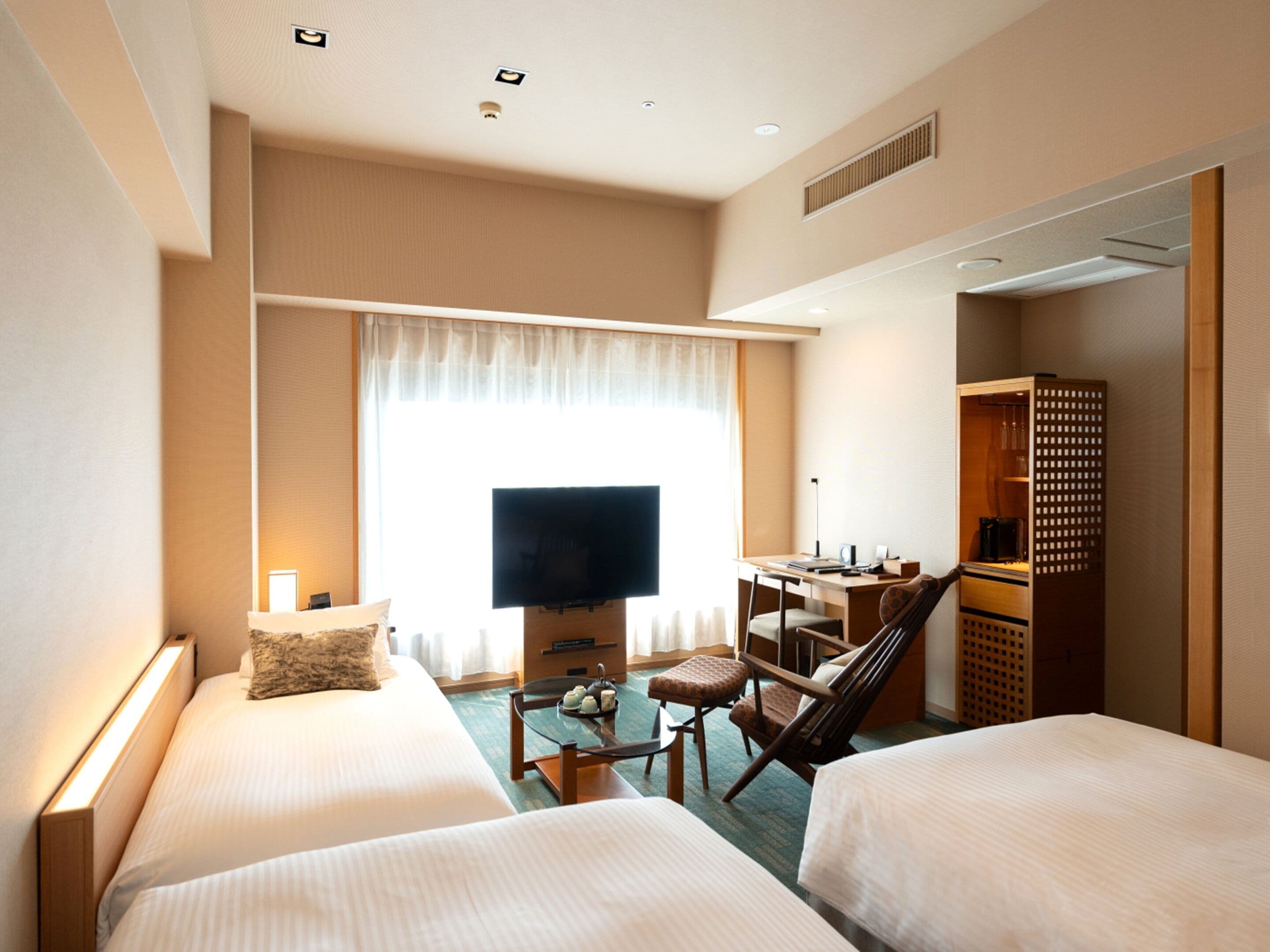 A hotel room with two beds, a desk, a chair, a television, and a wardrobe.