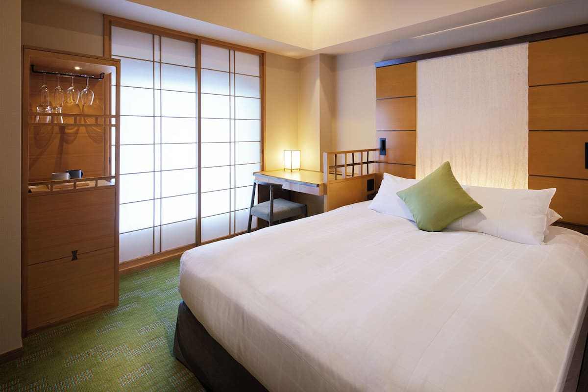 A hotel room with a bed, a desk, a chair, a wardrobe, and a sliding door.