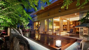 A modern outdoor pool area with wooden decking, seating, and a stone feature.