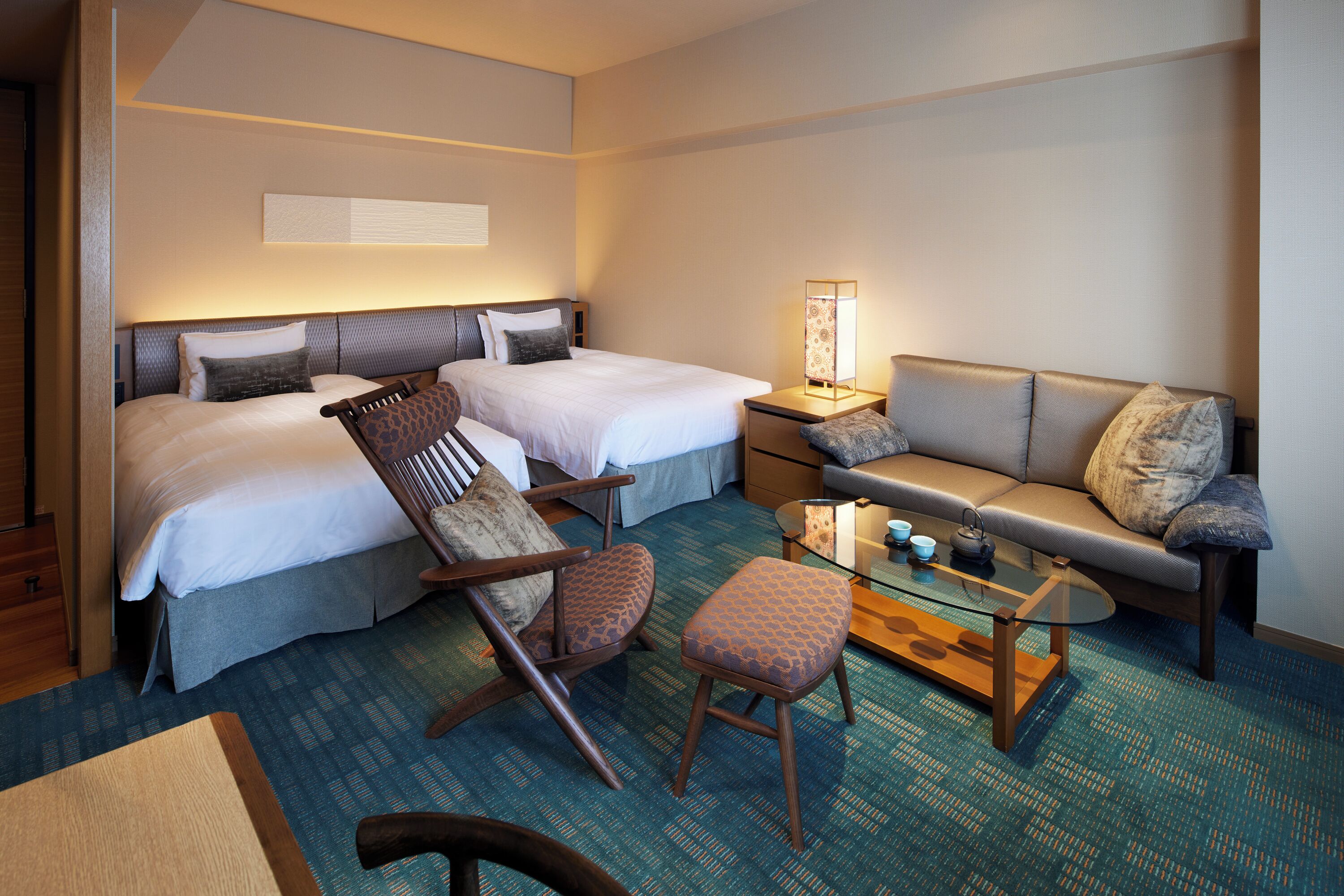 A hotel room with two beds, a sofa, a glass coffee table, and a chair.