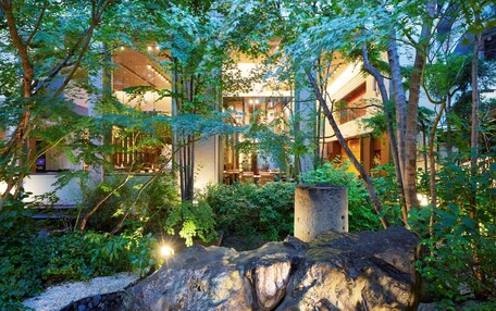 A serene garden with a waterfall, lush greenery, and a modern building with large windows.