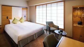 Quarto de hotel com uma cama grande, uma cadeira, uma mesinha com chá e um guarda-roupa cheio de roupas.