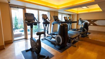 Una palestra con macchinari cardio, ampie finestre e pavimento in legno.