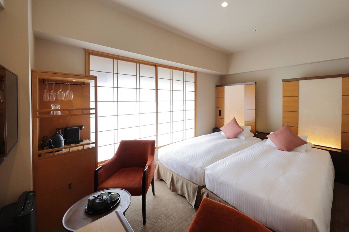 A hotel room with two beds, a seating area with a table, and a traditional Japanese sliding door.