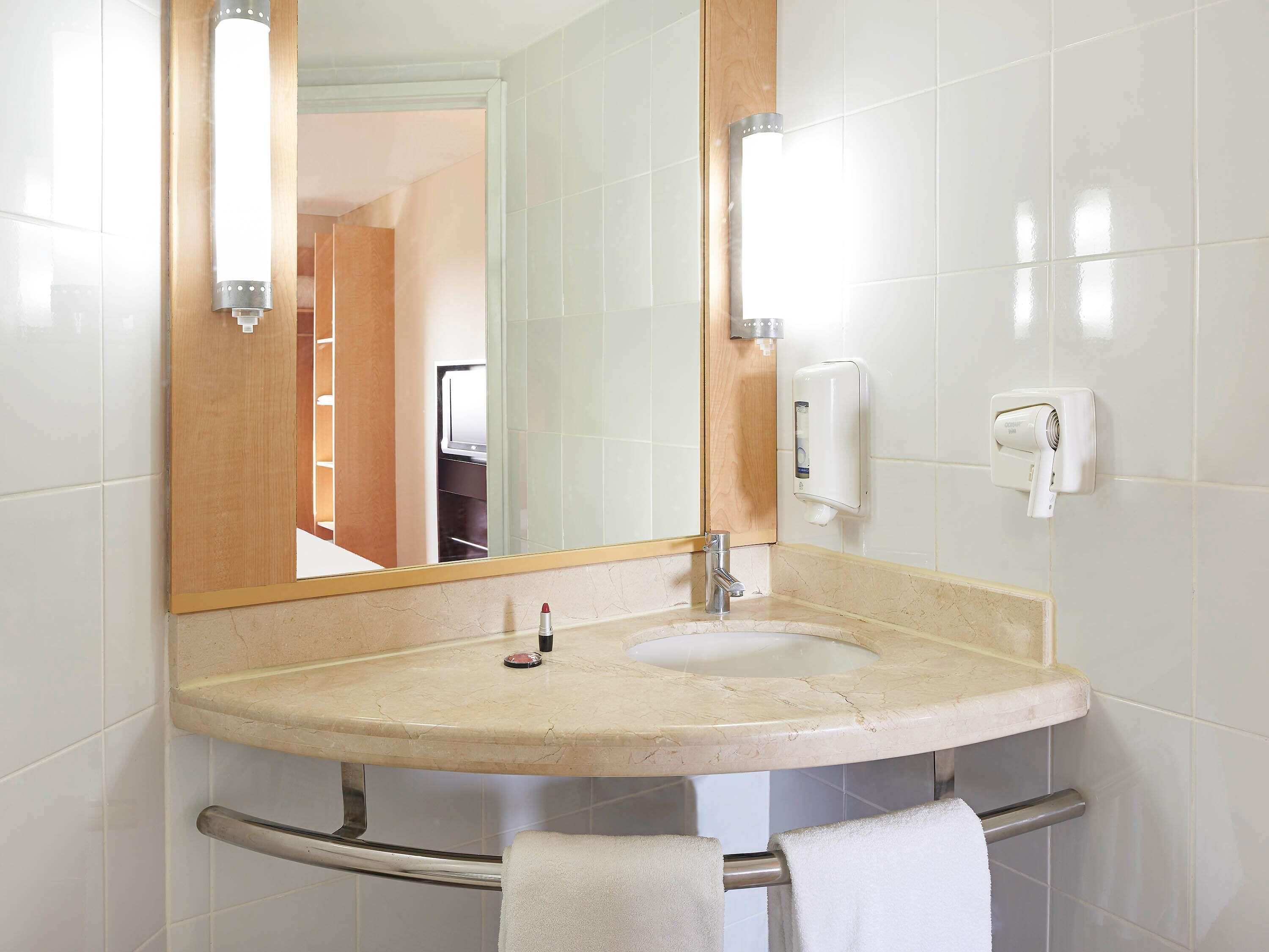 A bathroom with a sink, mirror, towel rack, and a hand dryer.