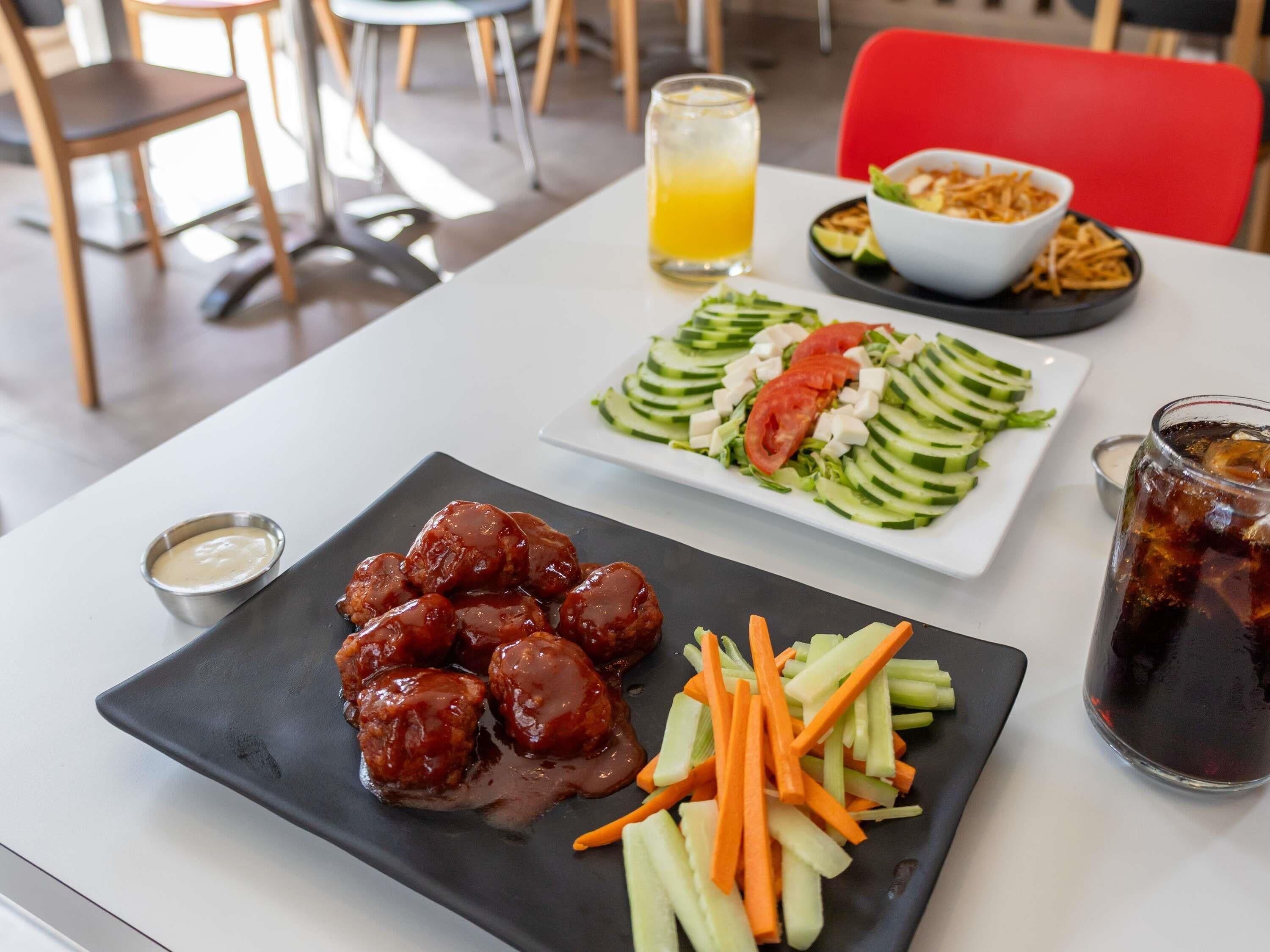 Uma mesa de jantar com um prato de almôndegas, uma salada e um copo de chá gelado.