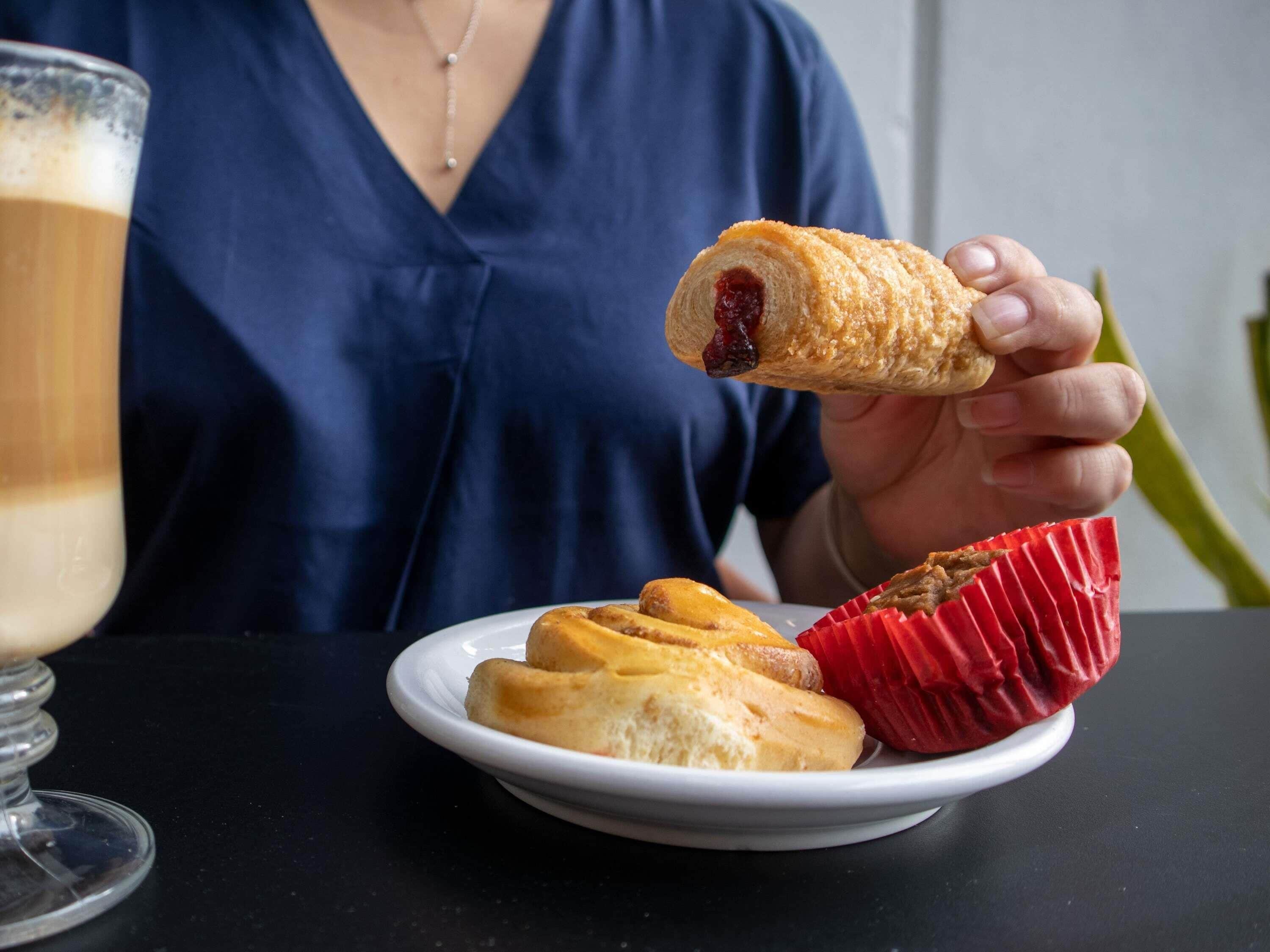 Una persona sosteniendo un pastelito con relleno rojo, un plato con dos pastelitos y un vaso de una bebida de color claro.