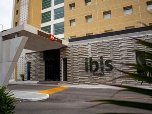 Fachada moderna de un hotel, con un letrero destacado de 'ibis Hotels' y un camino despejado hacia la entrada.