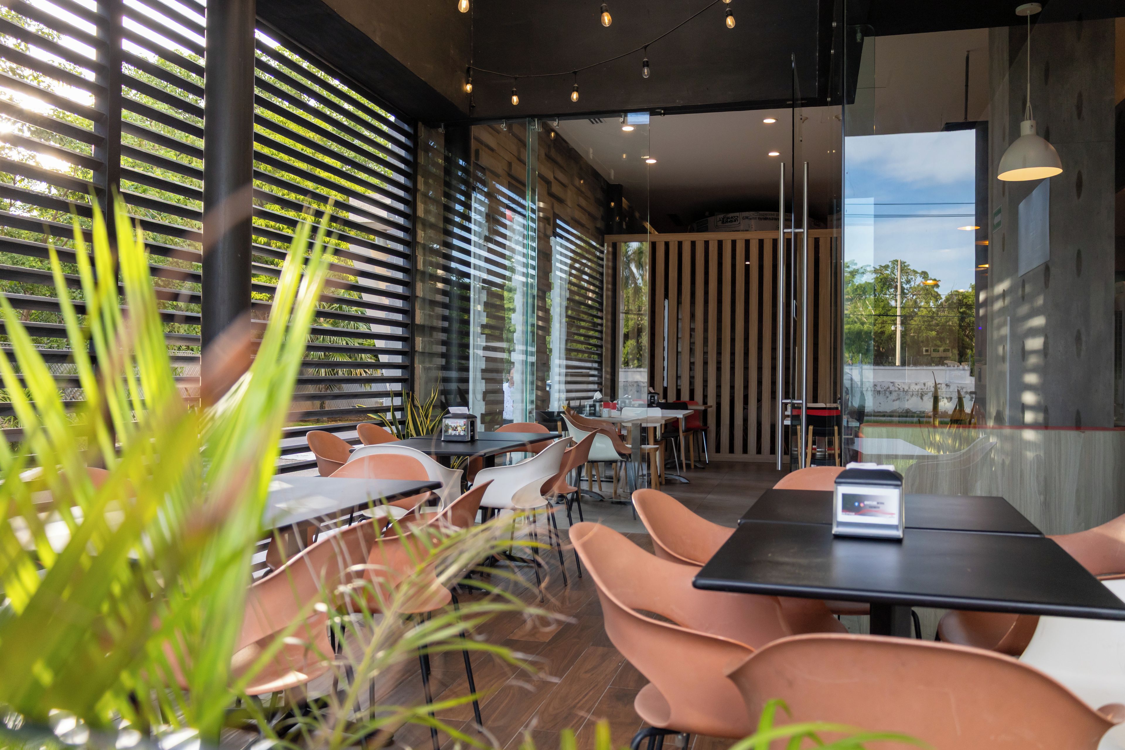 Un interior de restaurante moderno con mesas, sillas y vistas amplias por ventanas grandes.
