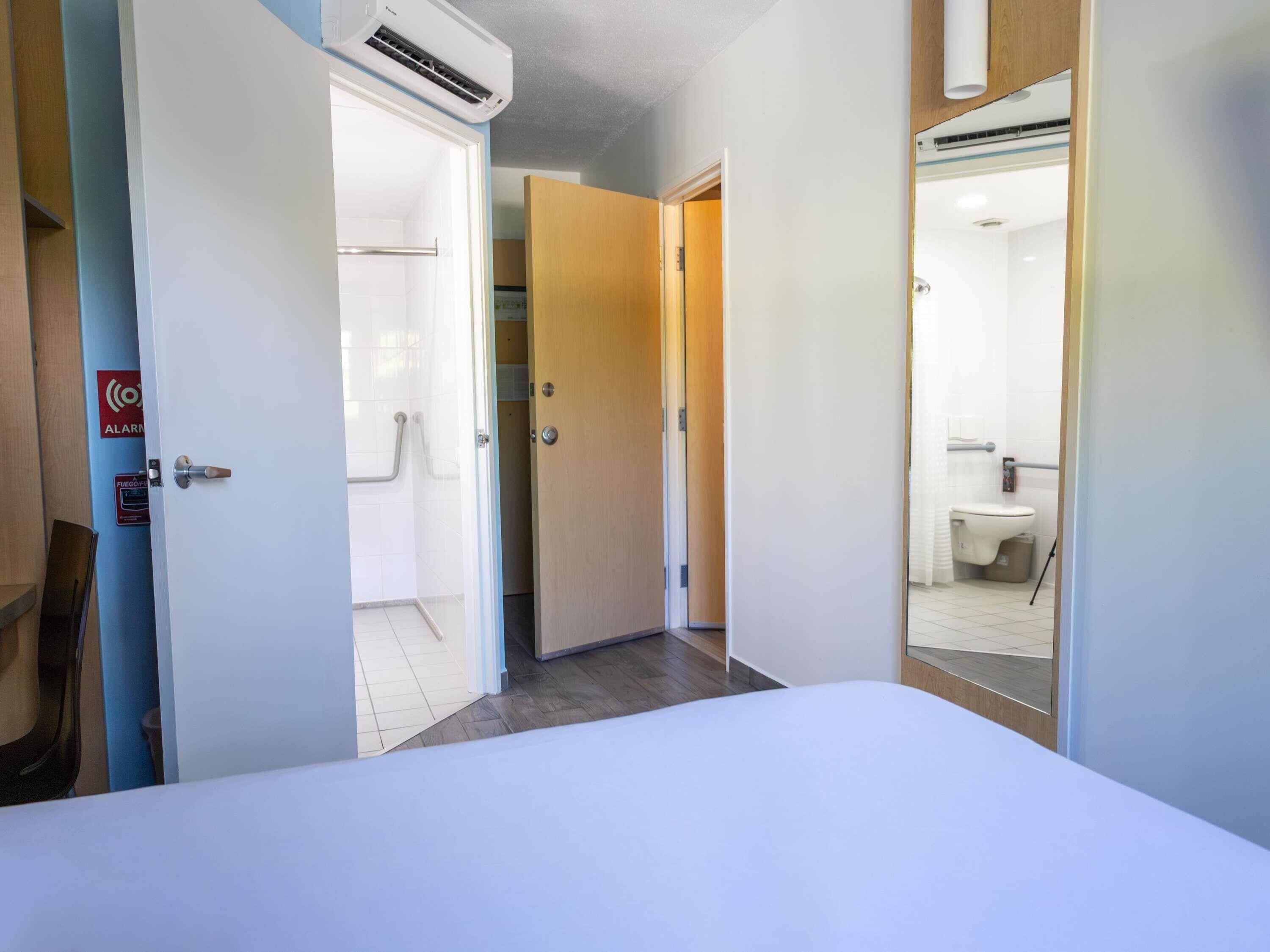 Quarto de hotel com cama, banheiro com vaso sanitário e pia, e área de chuveiro.