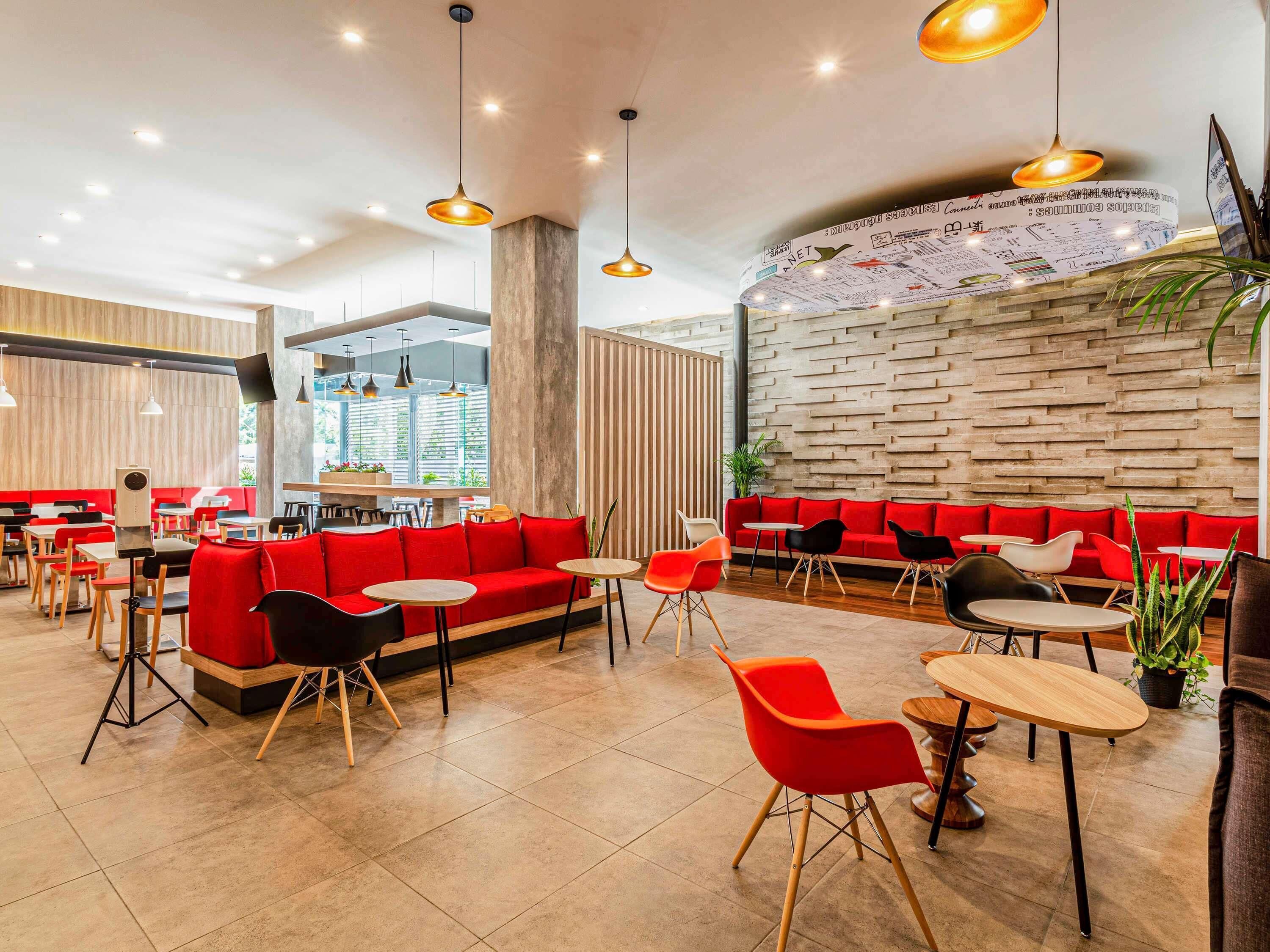 A modern restaurant interior with red seating, wooden tables, and hanging pendant lights.
