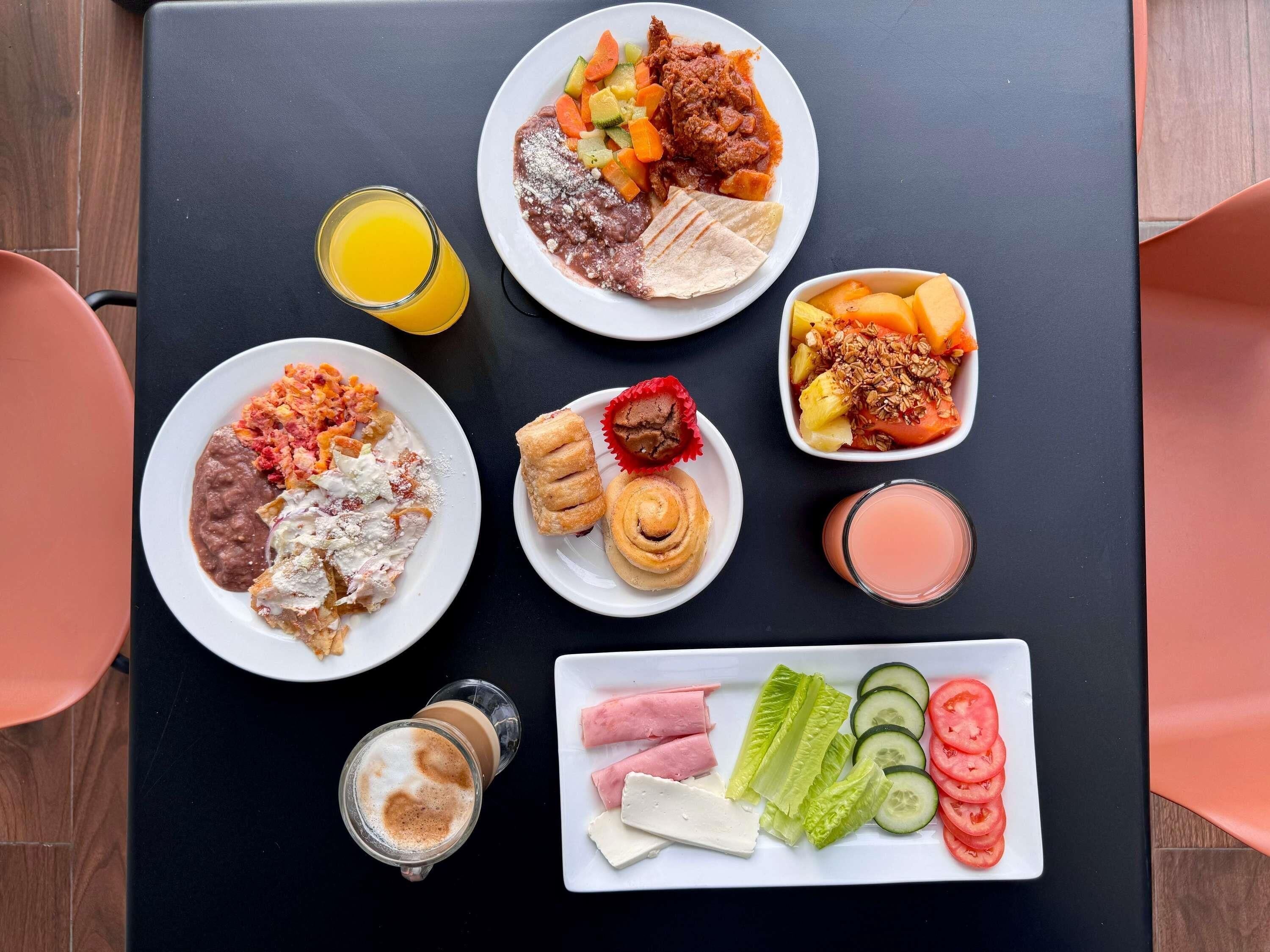 A table with various breakfast items including plates of food, a glass of orange juice, a glass of pink drink, and a plate with sliced vegetables and cheese.