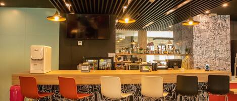 Uma área de bar com balcão, banquetas e geladeira.
