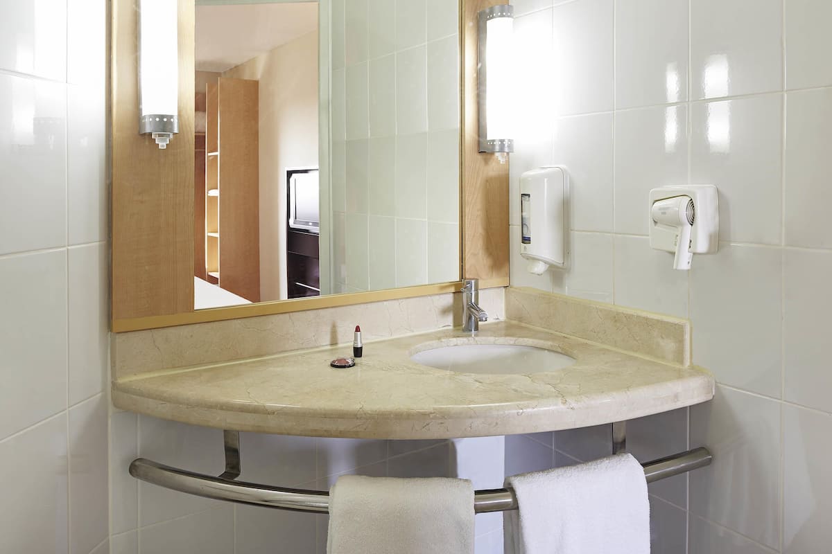 A bathroom with a sink, mirror, towel rack, and hand dryer.