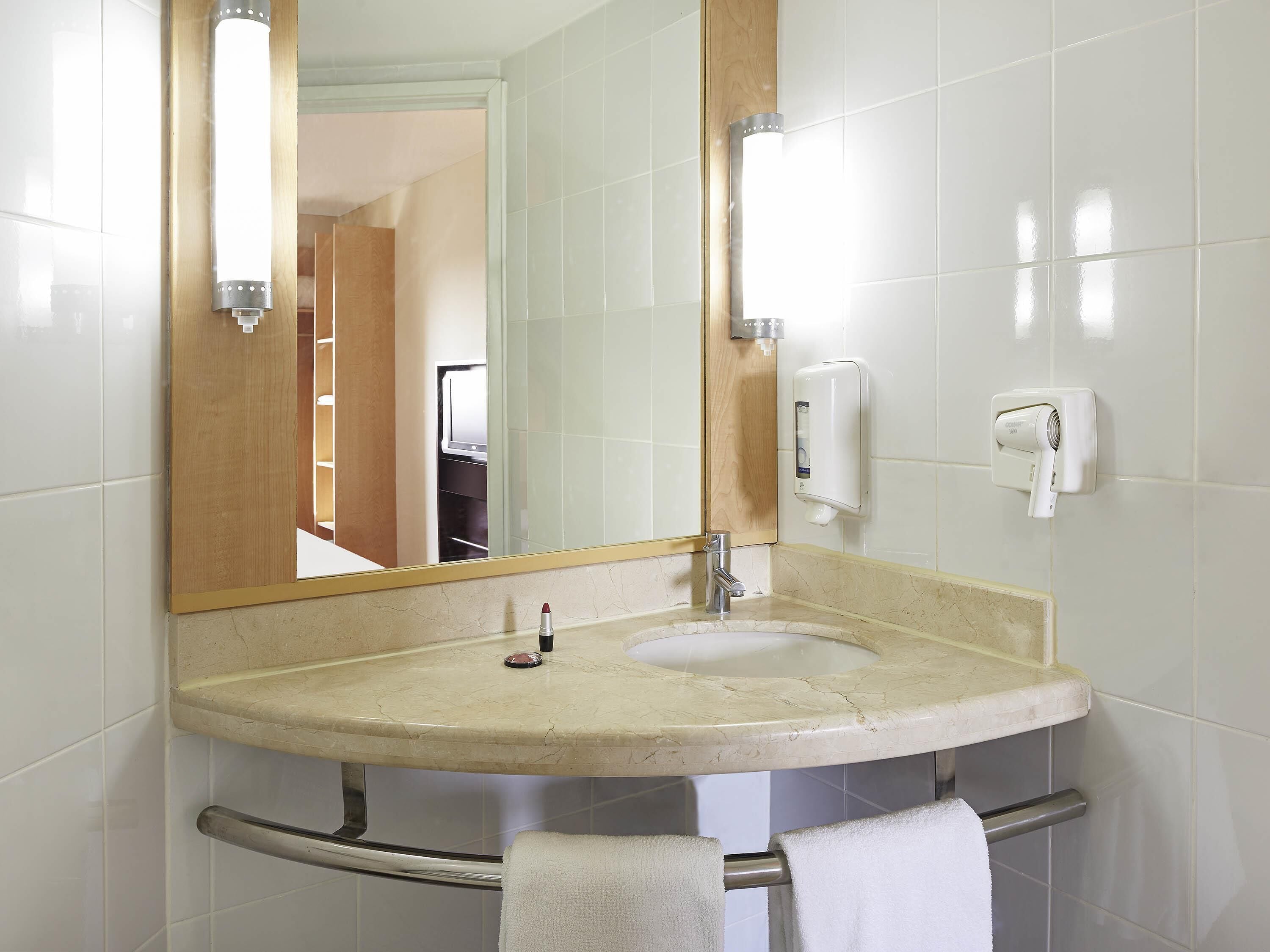 A bathroom with a sink, mirror, towel rack, and a hand dryer.