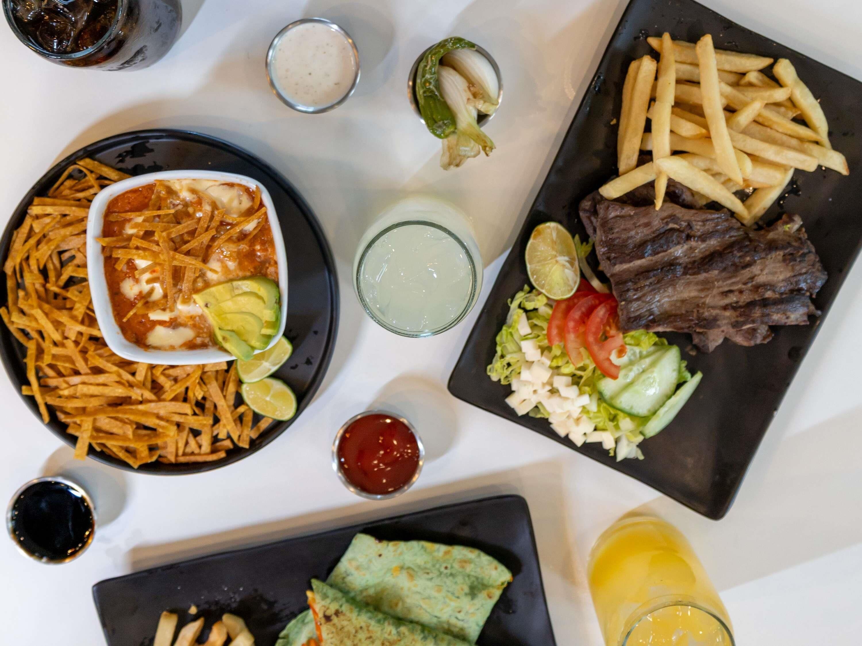 Una mesa con diferentes platillos, incluyendo nachos, papas fritas, carne a la parrilla y una ensalada.