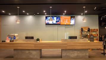 Un mostrador de recepción con un televisor de pantalla plana, una barra de madera y una planta en maceta.