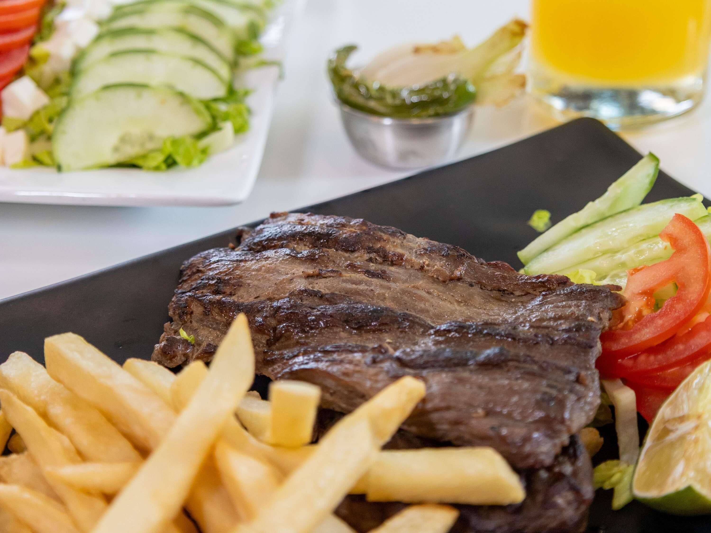 Un plato con bistec a la parrilla, papas fritas y una ensalada.