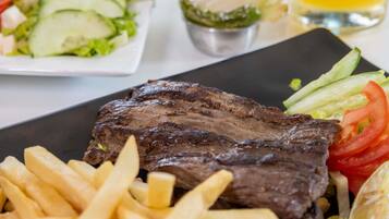 Un plato con bistec a la parrilla, papas fritas y una ensalada.