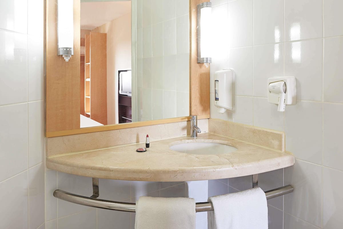 A bathroom with a sink, mirror, towel rack, and a hand dryer.
