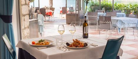 Un espacio de comedor al aire libre con una mesa dispuesta para dos, mostrando platos de mariscos y copas de vino.