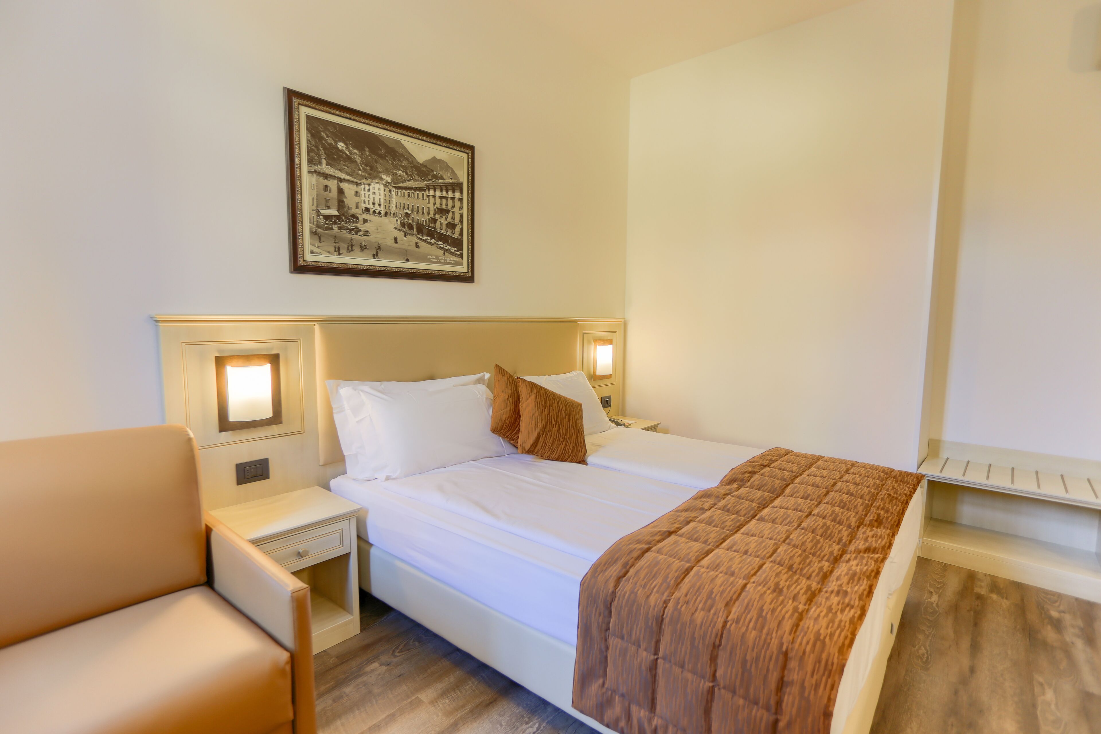 A hotel room with a bed, a nightstand, a chair, and a framed picture on the wall.