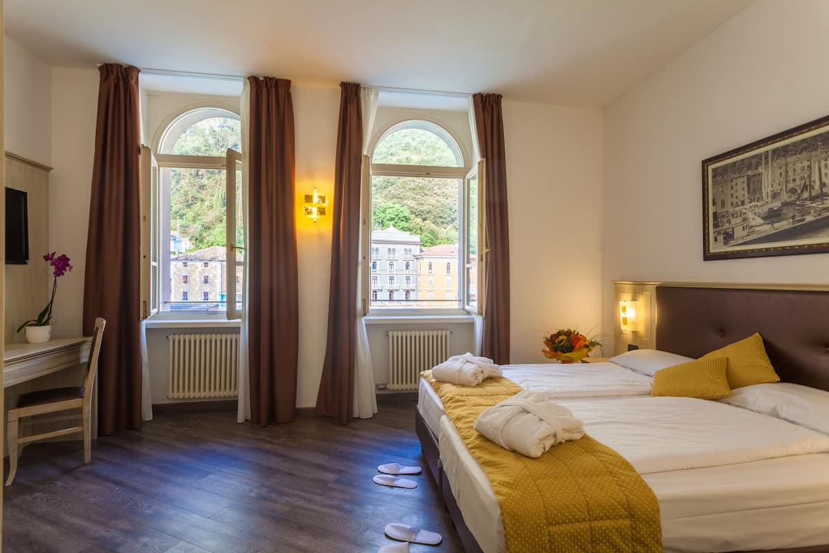 A hotel room with two beds, a desk, and a window with curtains.