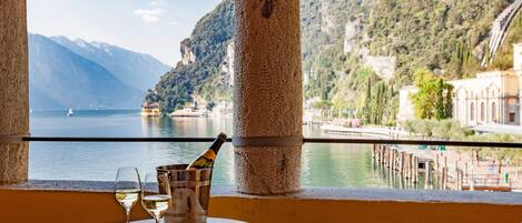 A table with a bottle of champagne, two glasses, and a key, overlooking a lake with mountains and buildings in the background.