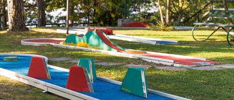 A miniature golf course with colorful obstacles and a picnic table in the background.